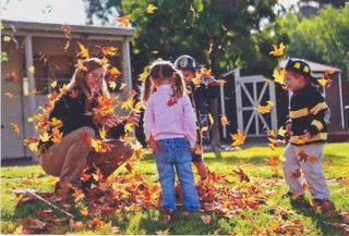 A woman playing with children in Autumn leaves.
