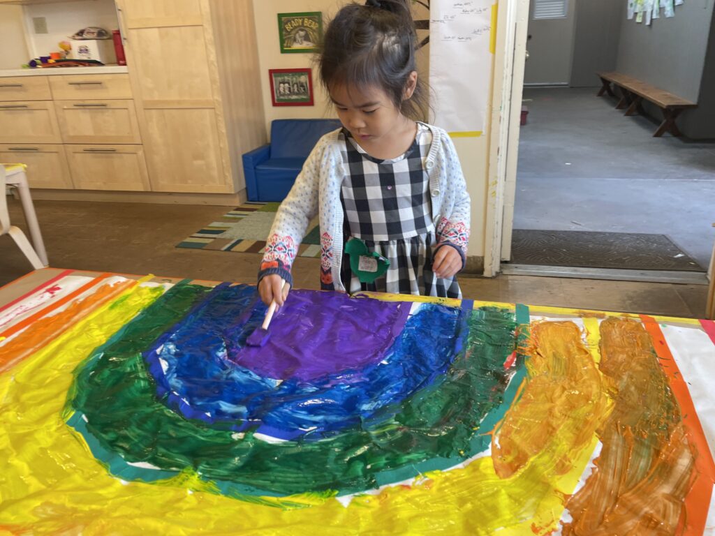 A little girl painting a big rainbow.