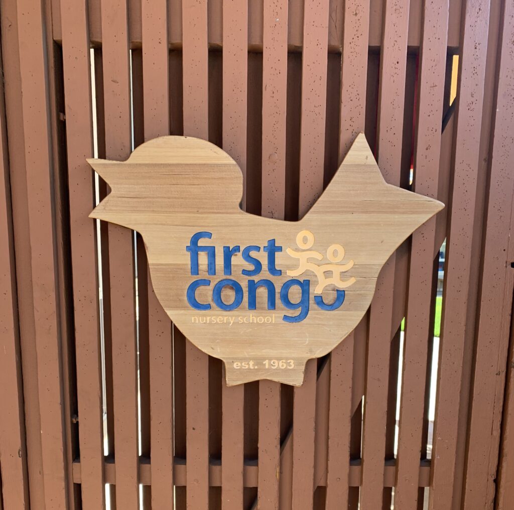 A wooden fence with a wooden bird cut out, the bird has the First Congo logo on it.