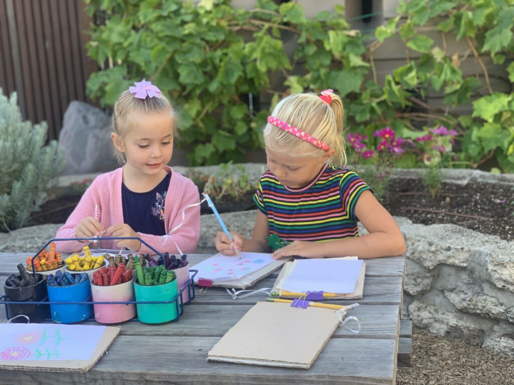 Two children drawing out plans on paper in a garden.